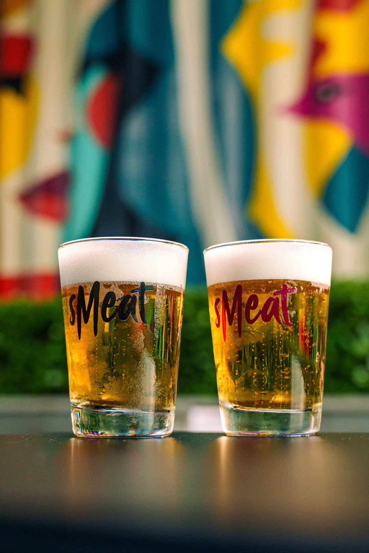 Dois chopps em copos do Smeat, com o mural da casa ao fundo
